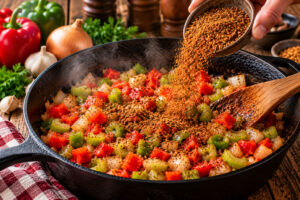 Cajun BBQ Gewürz wird über Paprika, Zwiebeln und Staudensellerie in einer gusseisernen Pfanne gestreut